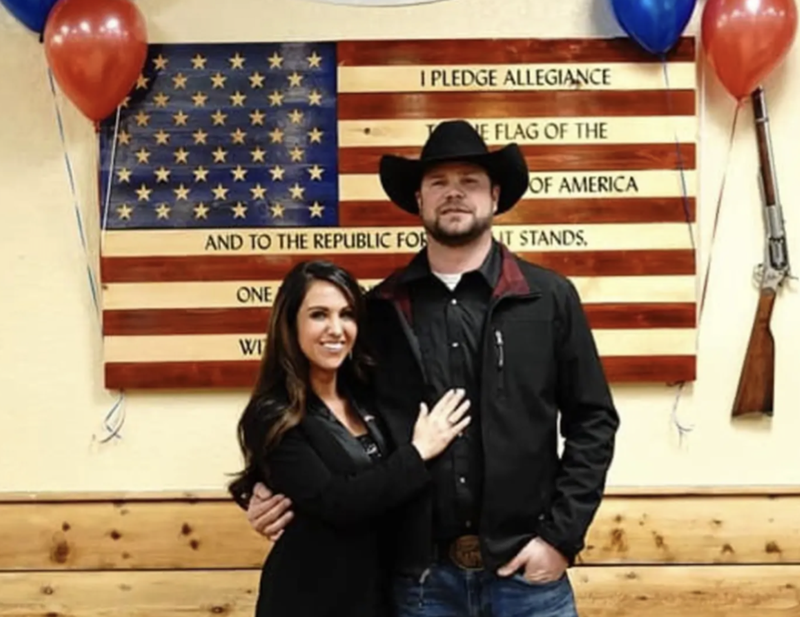Image: woman and man in cowboy hat in front of flag.
