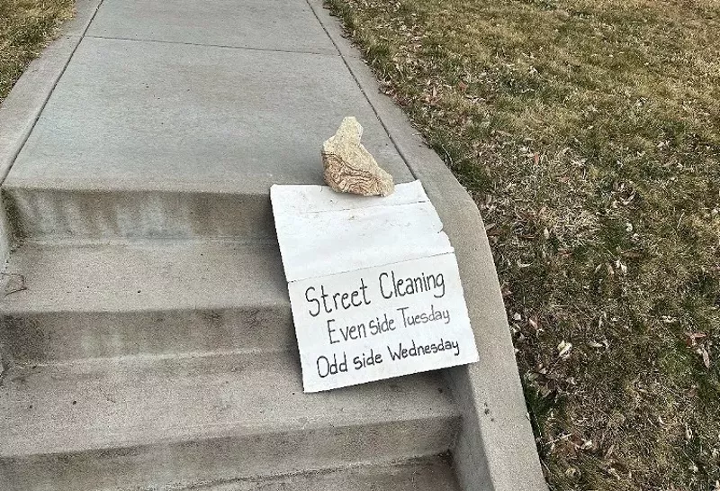 Image: rock on sidewalk steps with street-sweeping sign.