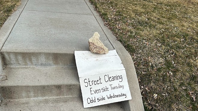 rock on sidewalk steps with street-sweeping sign.