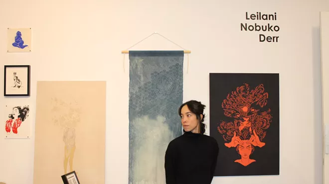 A woman poses in her studio in front of her artwork.