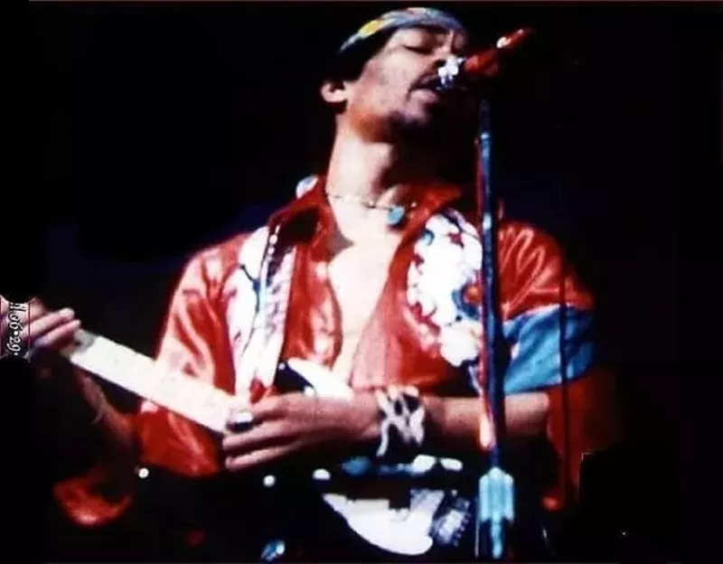 Image: Jimi Hendrix playing guitar in a red silk shirt