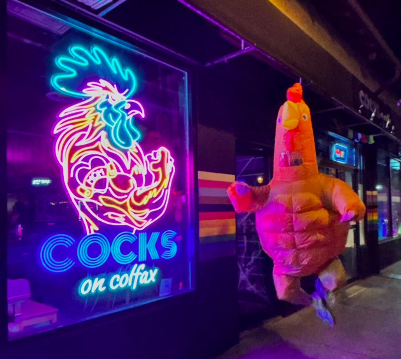 Image: person in a chicken suit next to a neon sign
