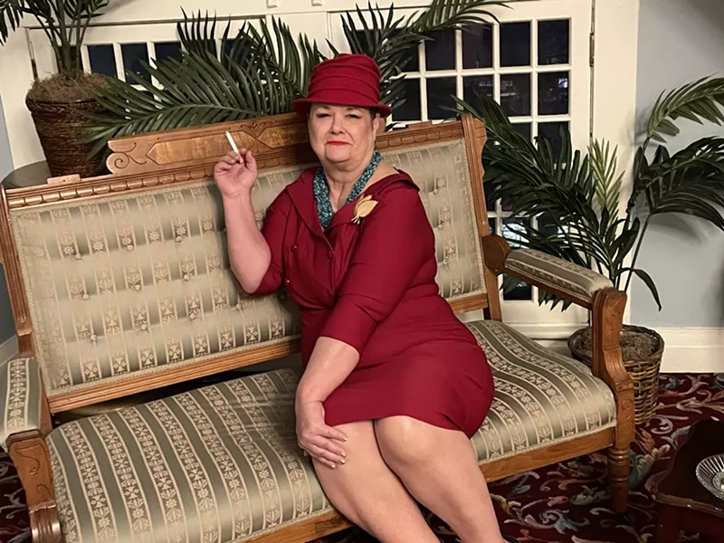 Image: woma in maroon dress and hat on sofa