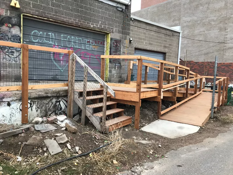 Image: A wheelchair ramp now replaces the old loading dock outside Rhinoceropolis and Glob. A tribute to the late Colin Ward is spray-painted on the garage.