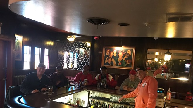a man in an orange hoodie stands behind a bar where patrons are seated