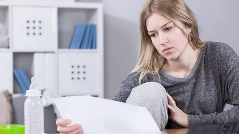Image: A blonde woman gazes at a document with a perturbed expression.