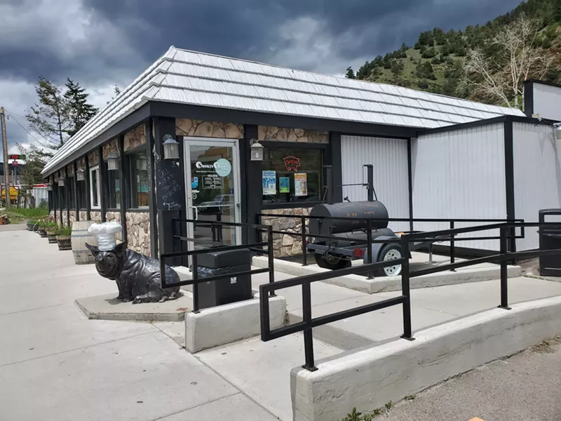 Image: a small building with a pig sculpture and a smoker out front