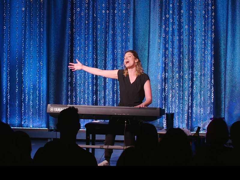 Image: woman at piano in front of curtain.