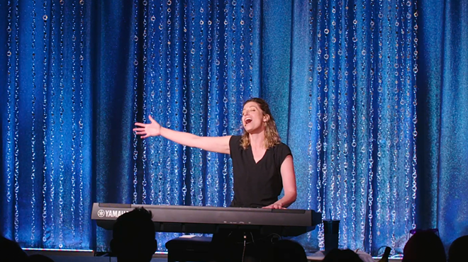 woman at piano in front of curtain.