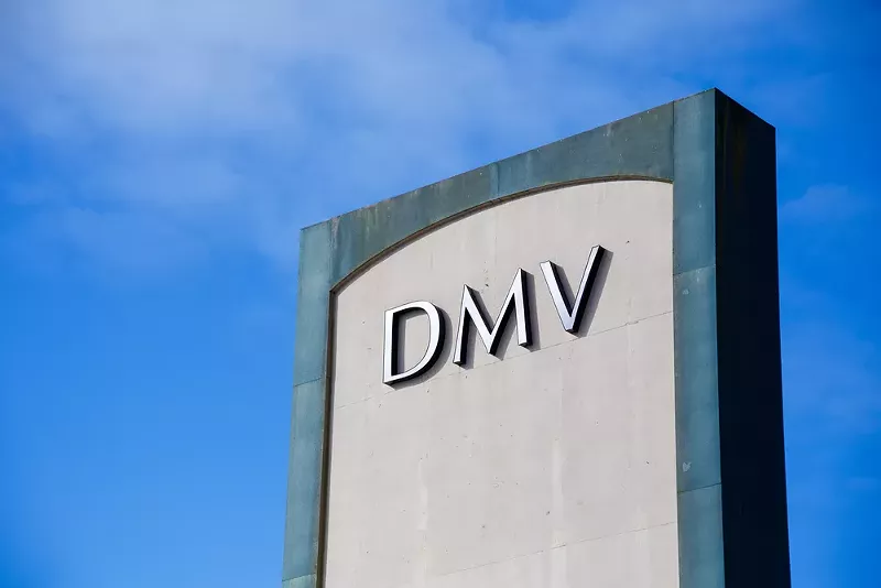 Image: A DMV sign outside against a blue sky.