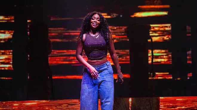 R&B singer SZA in blue pants on stage with an orange background