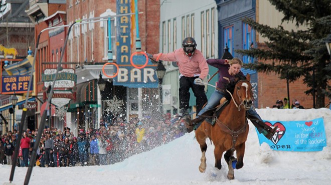 woman on horse pulling skier down snowy Western street