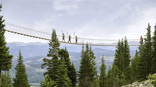 Three people backdropped by mountains while crossing the aerial bridge at Breckenridge Ski Resort
