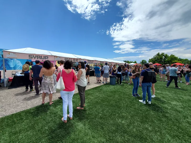 Image: people standing on grass waiting in line at a food fest