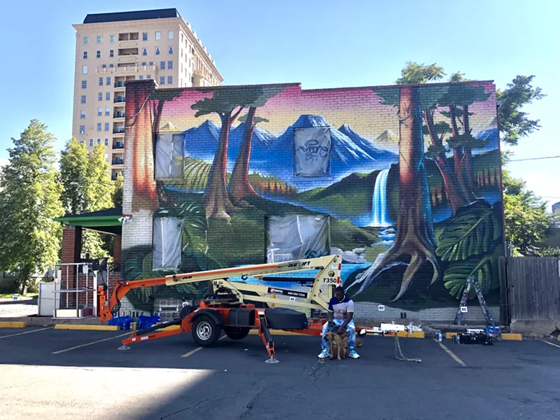 Image: Robert Gray sits in front of a mural painted by artists Tuke One and Chad Bolsinger at the dispensary Higher Grade on Elati Street. Gray connected the dispensary owners with the mural artists.