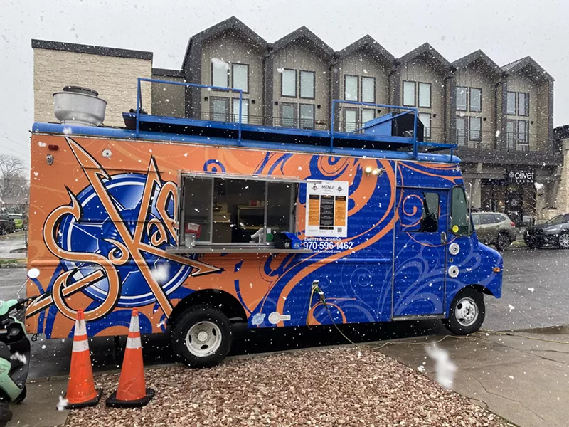 Image: a food truck with a blue and orange wrap.