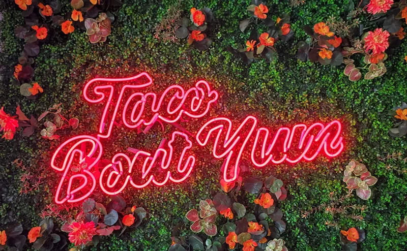 Image: a neon sign in front of a leafy wall