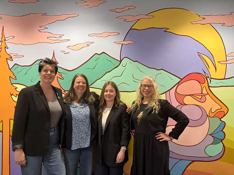 Image: women in blazers smile in front of a mural