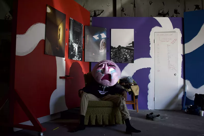 Image: Person in chair with large crying mask.
