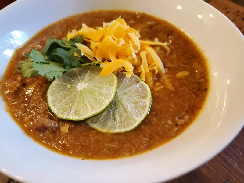 Image: a bowl of green chile with limes, cheese and cilantro on top