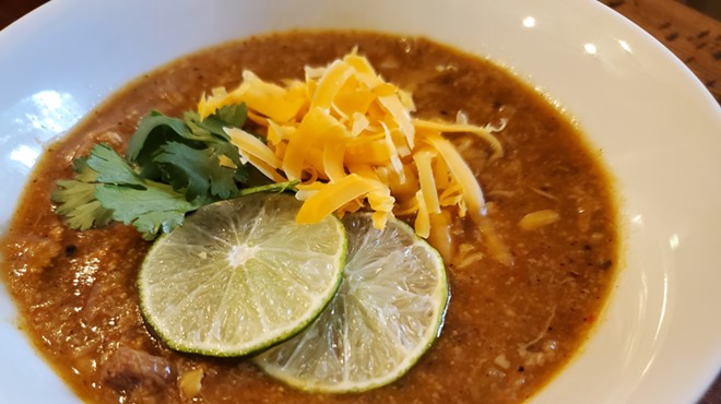 a bowl of green chile with limes, cheese and cilantro on top