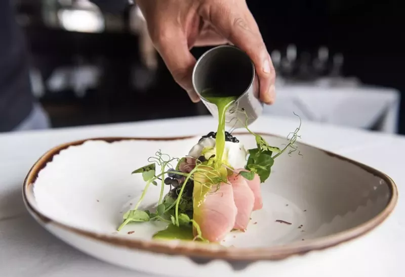 Image: A hand pouring cucumber leche de tigre on hamachi