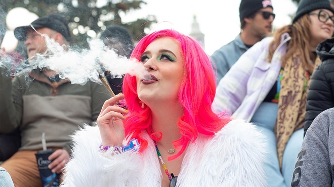Woman with pink hair and white fur coat smokes weed