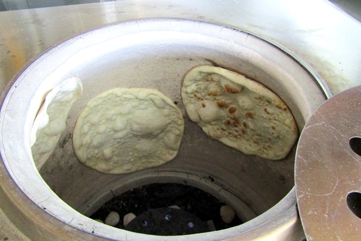 Dough is stretched and pressed against the clay inner wall of a tandoori oven. - MARK ANTONATION