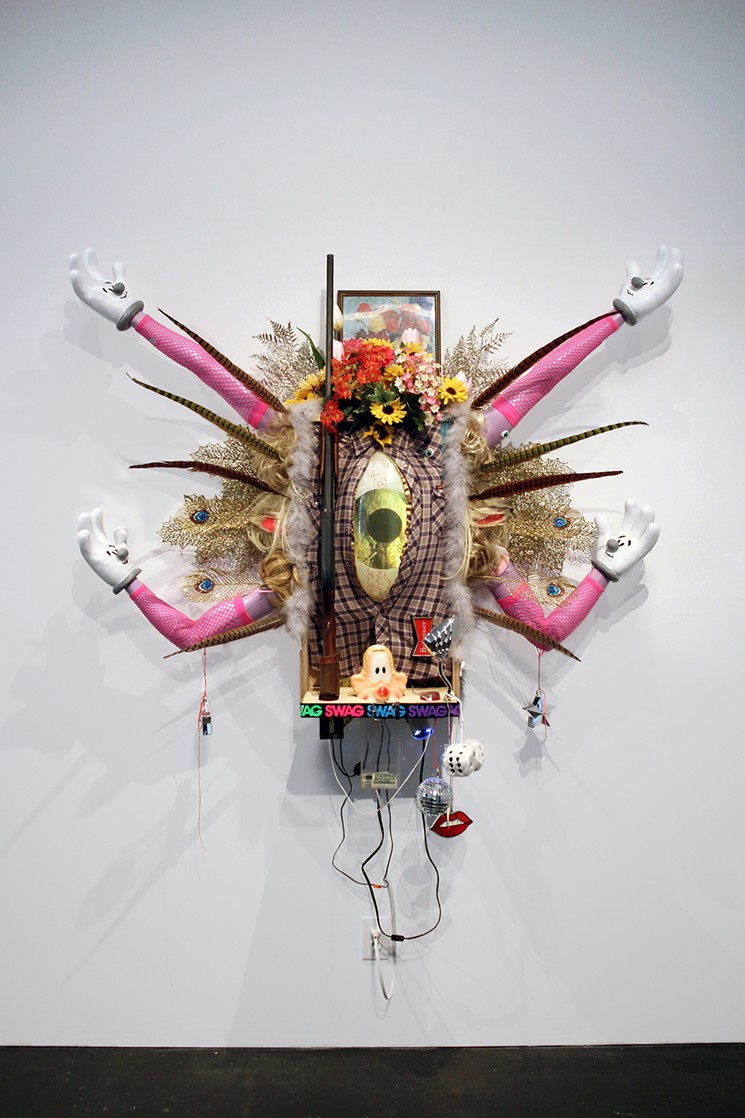 Donald Fodness, “Swag Emission,” 2016, bondo, plastic resin, acrylic paint, spray paint, mannequin arms, steel, birch plywood, Lee brand flannel shirt, boa, pheasant feathers, fake glitter peacock feathers, fake glitter leaves, fake flowers, flower, plexiglass, plaster, belt, felt, 20 gage shotgun, lenticular photograph in metal frame with printed wood finish, faux wood grain tape, led lamp, beer lamp, disco balls, blouse, concrete, wire, baked resin lips, netted fingerless gloves, magnets, thumbtacks, plastic eyes, superglue, star weight, mason string, eyelets, screws, marker, gesso, electrical chords, auxiliary jack, wigs, speakers, fuzzy dice, motorcycle mirror. - COURTESY OF DONALD FODNESS
