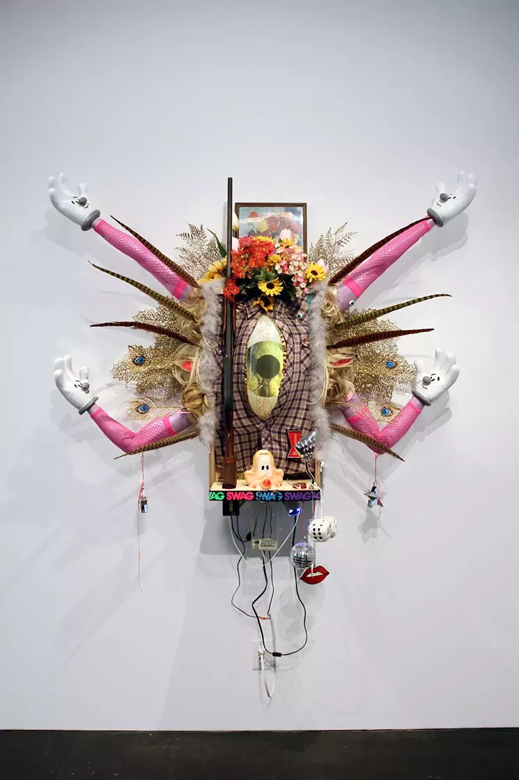 Donald Fodness, “Swag Emission,” 2016, bondo, plastic resin, acrylic paint, spray paint, mannequin arms, steel, birch plywood, Lee brand flannel shirt, boa, pheasant feathers, fake glitter peacock feathers, fake glitter leaves, fake flowers, flower, plexiglass, plaster, belt, felt, 20 gage shotgun, lenticular photograph in metal frame with printed wood finish, faux wood grain tape, led lamp, beer lamp, disco balls, blouse, concrete, wire, baked resin lips, netted fingerless gloves, magnets, thumbtacks, plastic eyes, superglue, star weight, mason string, eyelets, screws, marker, gesso, electrical chords, auxiliary jack, wigs, speakers, fuzzy dice, motorcycle mirror. - COURTESY OF DONALD FODNESS