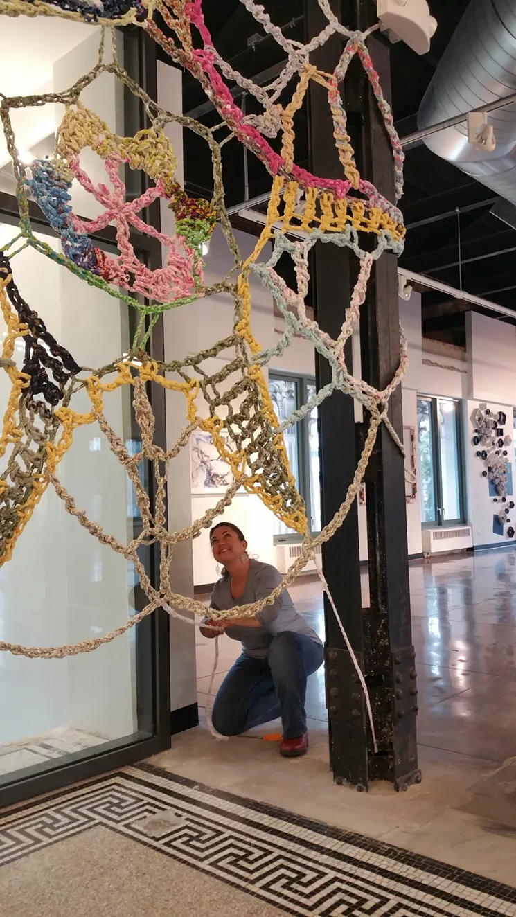 Angela Beloian installing "Safety Net," a work created from braided and crocheted bed sheets in response to refugees fleeing their homelands. McNichols Building, Denver, 2017. - PHOTO COURTESY OF JIM WALKER