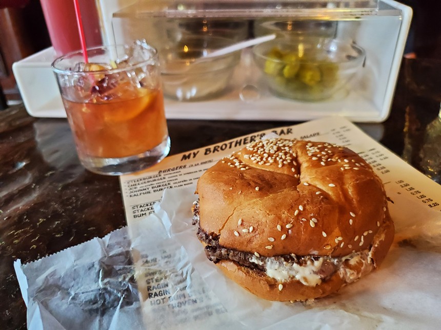 a cheeseburger with a sesame seed bun in front of an old fashioned cocktail