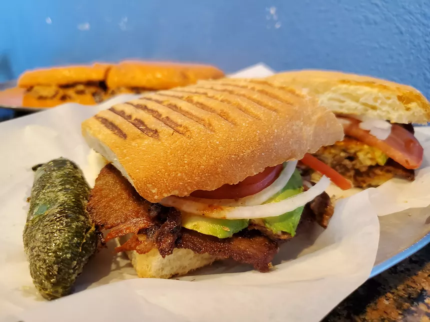 a jalapeno next to a sandwich with meat, avocado, onion and tomato