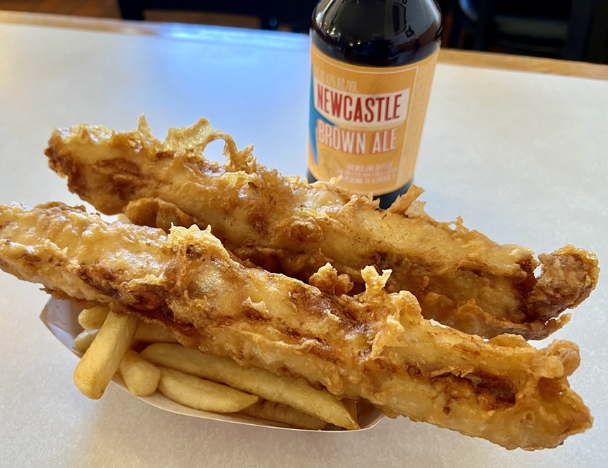 two pieces of fried fish on french fries next to a bottle of beer