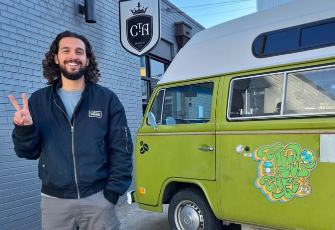 man in a dark jacket stands next to a green VW van.