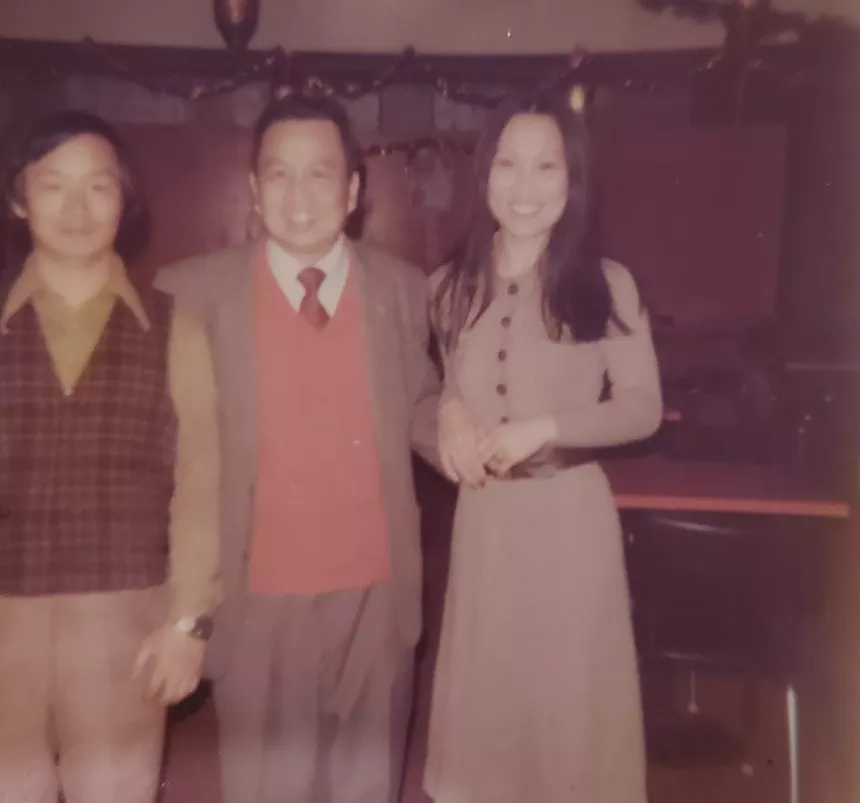 two men stand next to a woman in a tan dress
