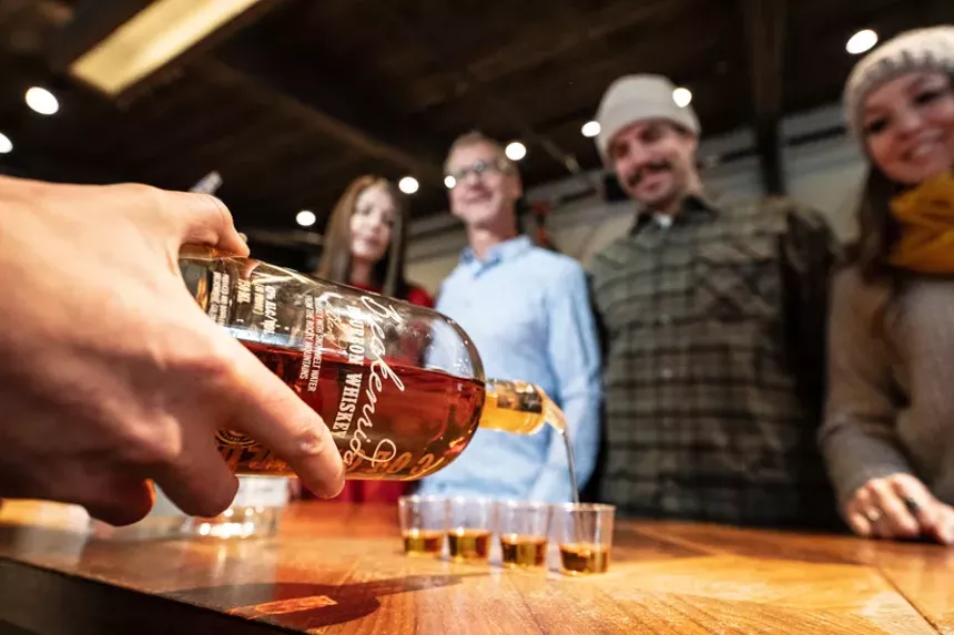 a hand holding a bottle of whiskey, pouring shots as three people watch