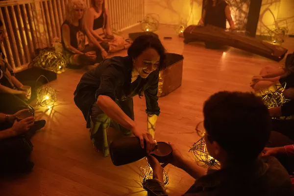 a woman kneels on the ground and pours liquid into a cup