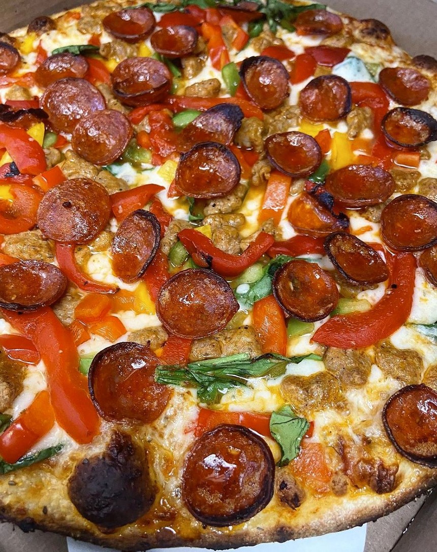 a pizza topped with pepperoni, peppers, basil and sausage.