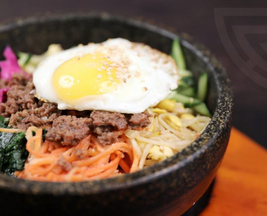 a fried egg on top of meat and vegetables in a stone bowl