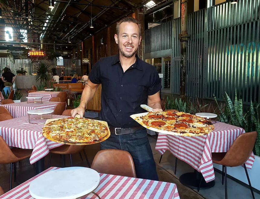 a man holding two whole pizzas on trays