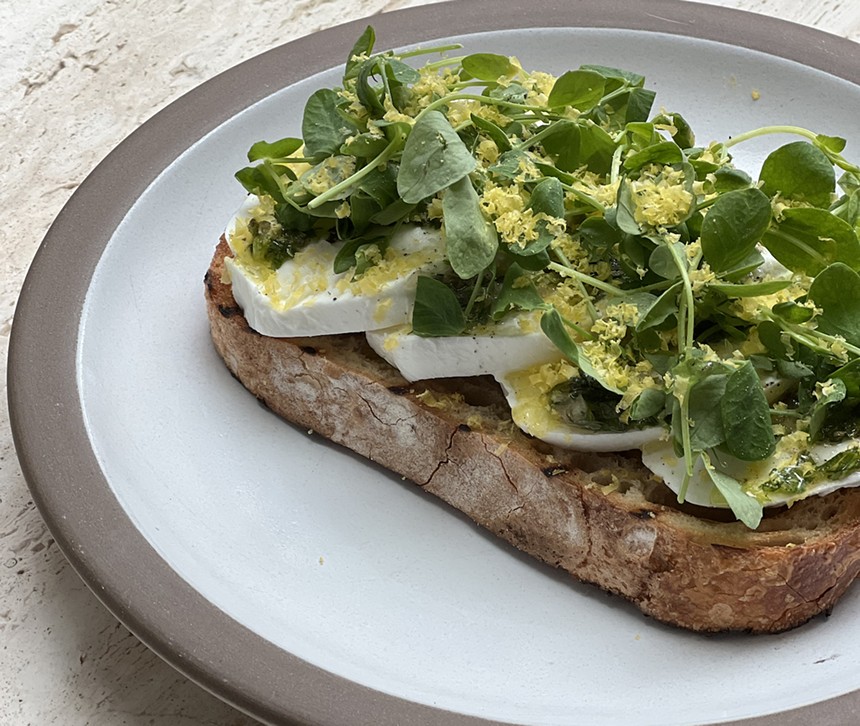 A bread slice on a plate with mozzarella cheese and greens.