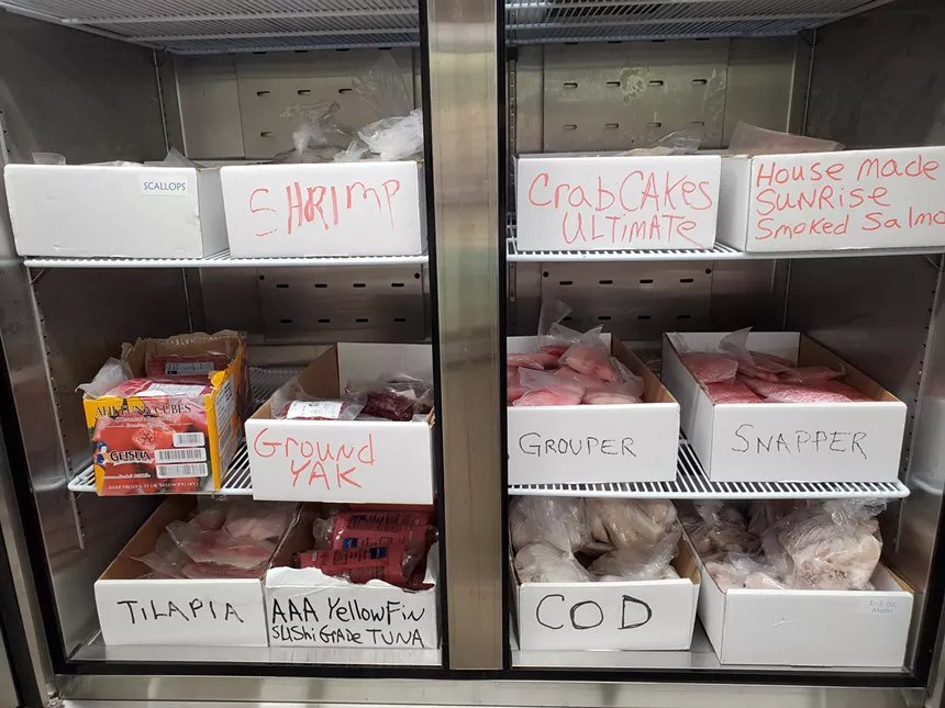 an open freezer stocked with boxes of fish