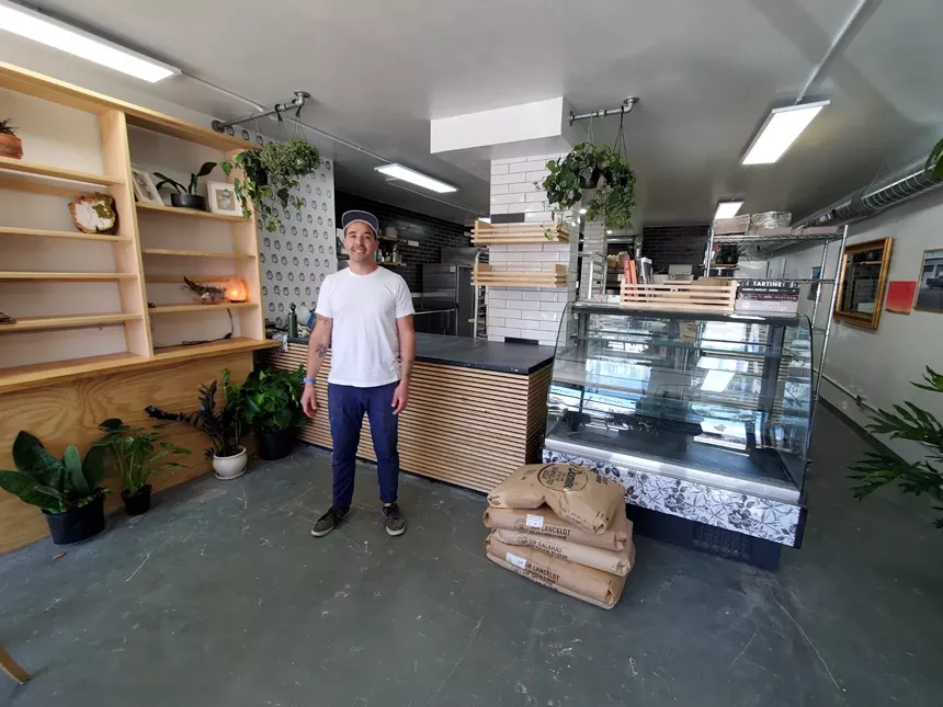 a man stands in a shop with shelves and a counter behind him
