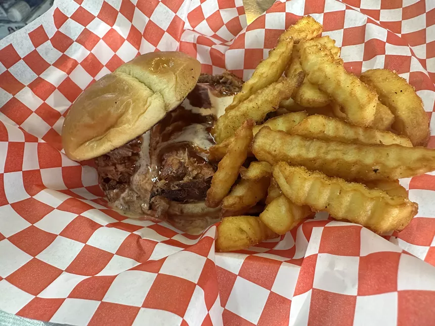 a pulled pork sandwich and fries on red and white checkered paper.