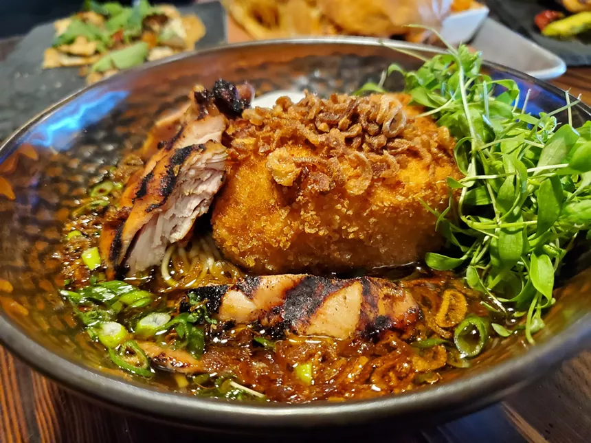 a bowl of ramen with chicken and a fried potato croquette