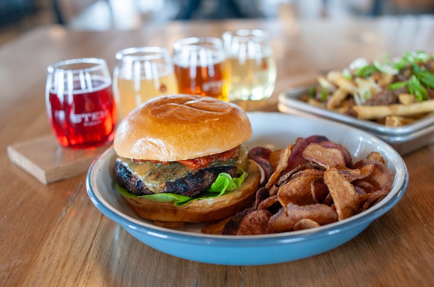 Burger and chips on a plate in front of a flight of cider in glasses