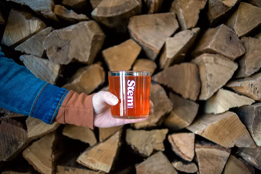 Cider in a hand with wood logs in background.