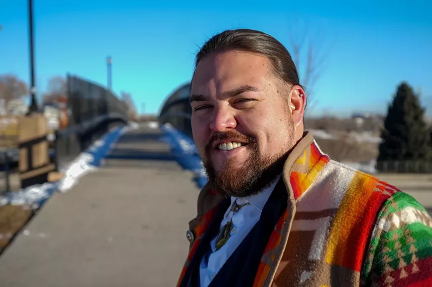 Ean Tafoya wears a tan coat with orange and red designs, similing at the camera.