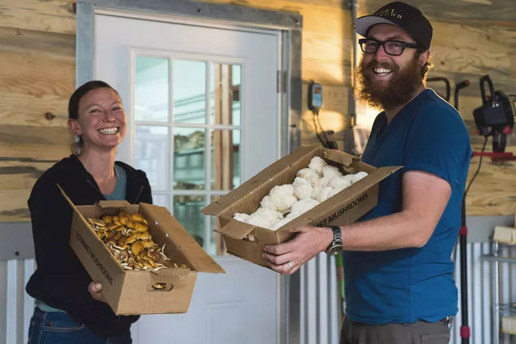 two people stand in front of a door holding boxes filled with mushrooms